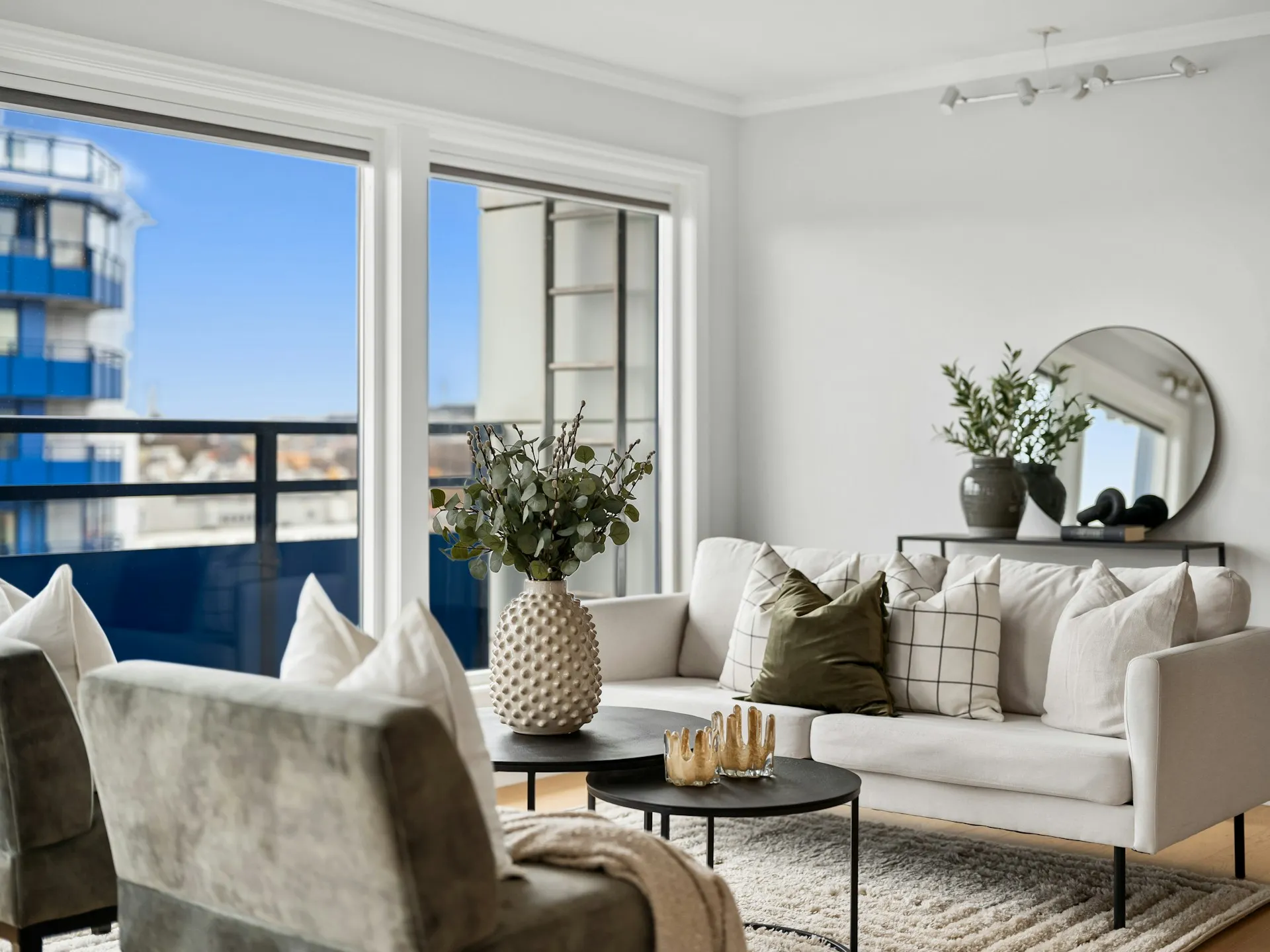Living room with a gray sofa, round table, decor, and large windows with balcony view.