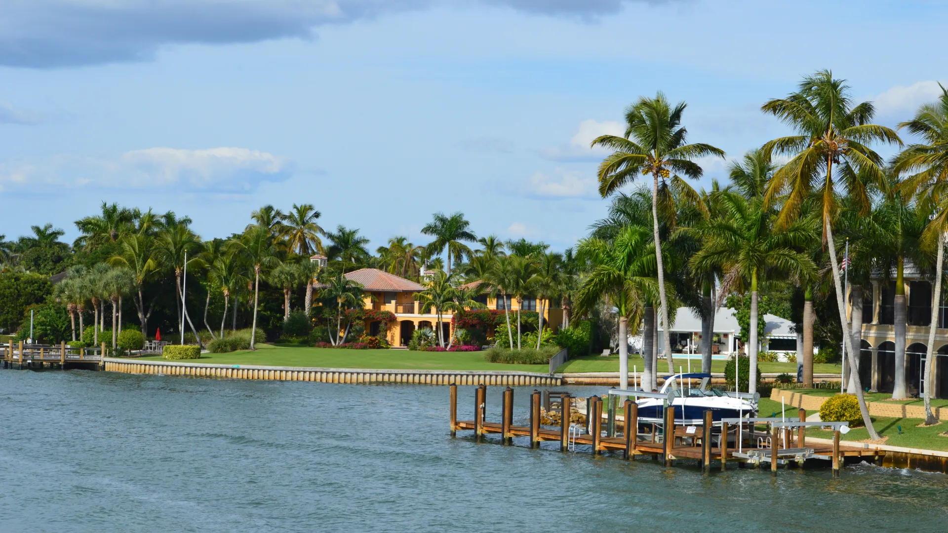 Luxury California real estate houses with lawns, palm trees, and a boat dock by lake
