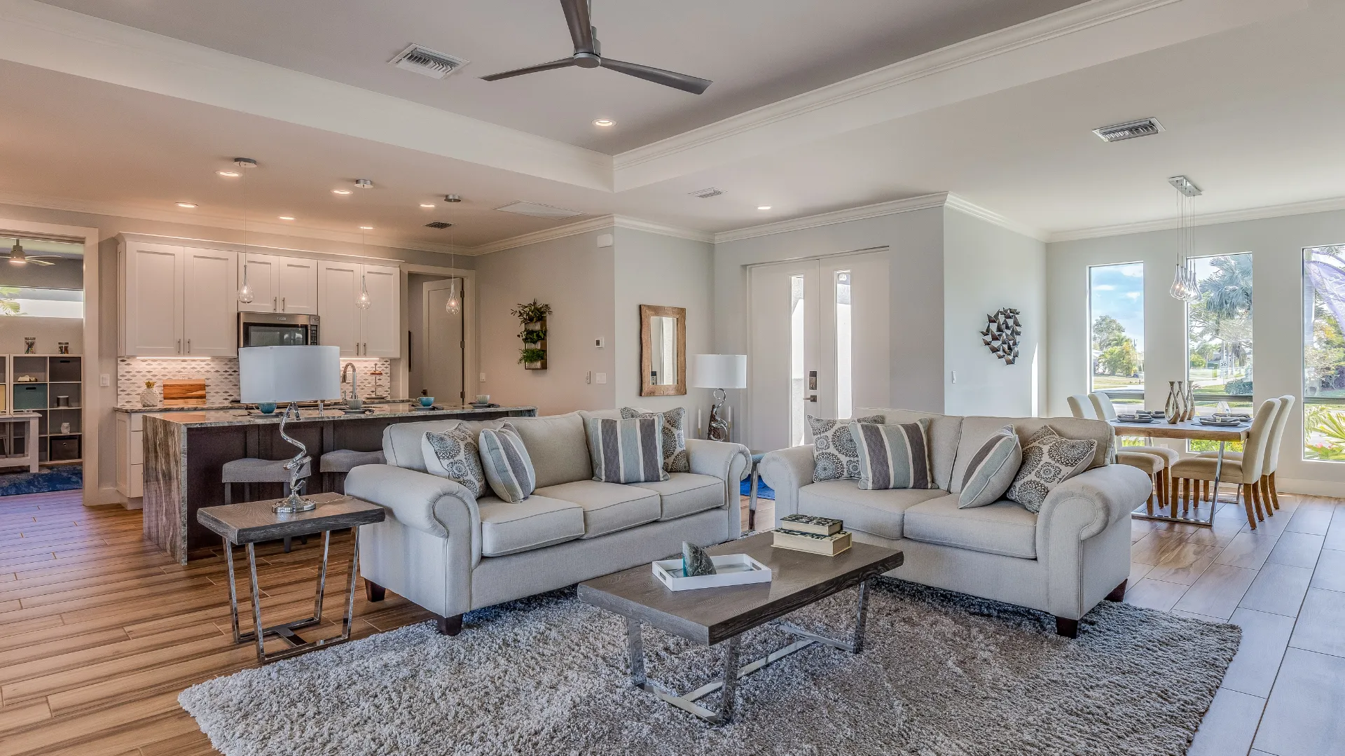 Living room with a sofa, coffee table, decor, kitchen, dining table, and large windows.