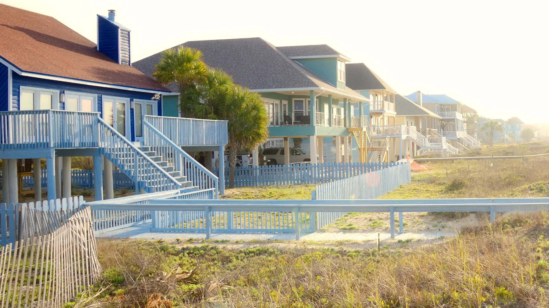 California real estate houses with colorful walls, wooden walkways, sand, and plants.