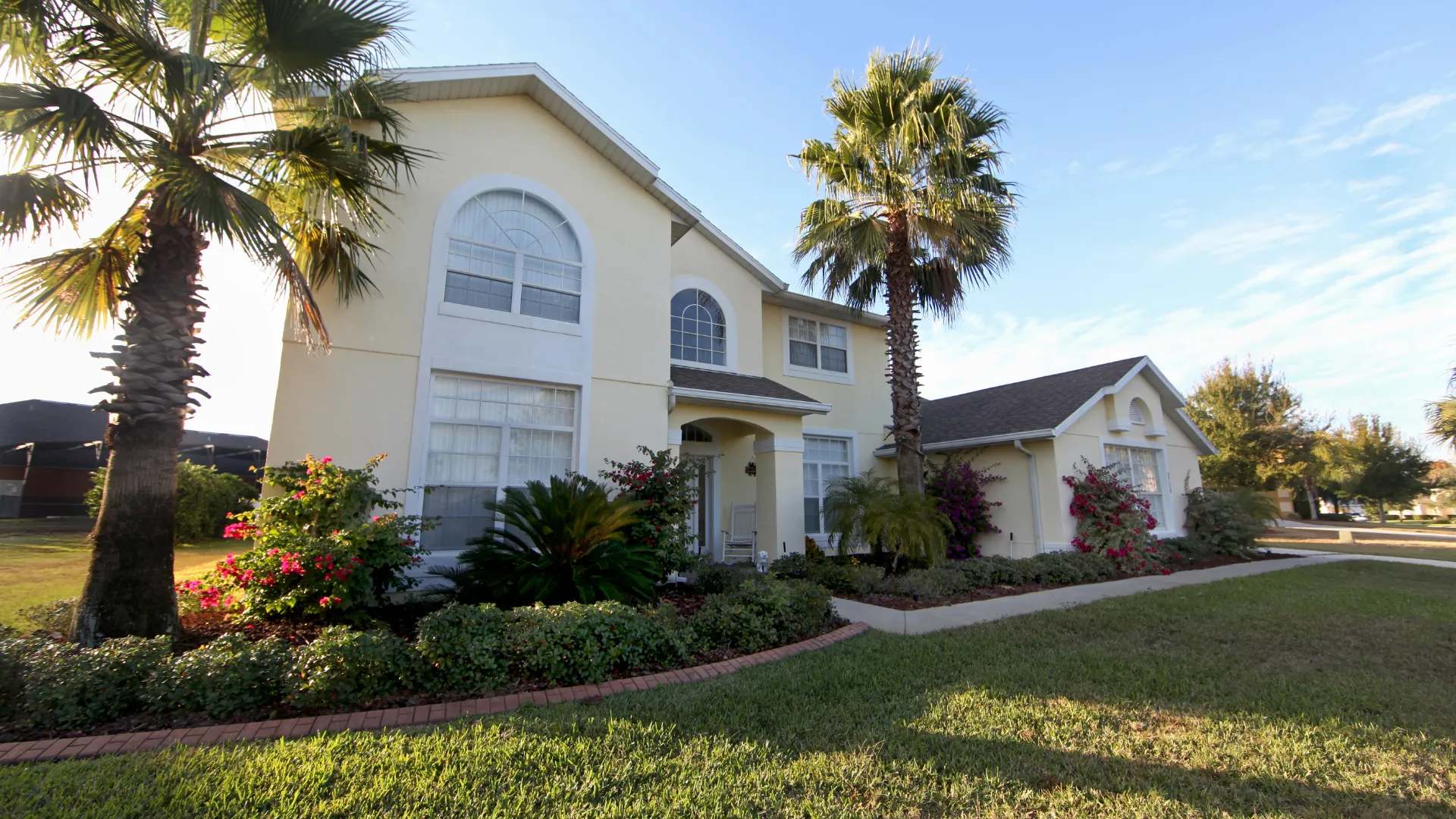 California real estate house with two floors, palm trees, flowers, and green plants.